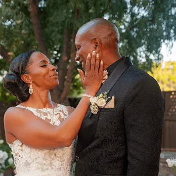 Bride gently holding groom's face while smiling at him during an outdoor wedding ceremony.