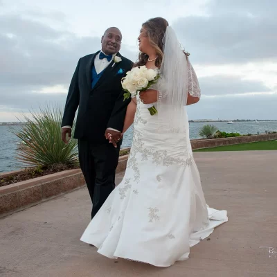 Bride and groom holding hands and smiling while walking along a waterfront path on their wedding day