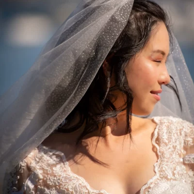 Bride wearing lace wedding gown and sheer veil, smiling while standing outdoors