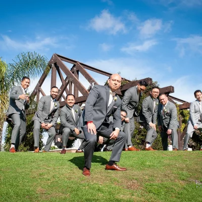 Groom in grey suit posing with groomsmen outdoors on a sunny day with blue sky and palm trees