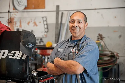Experienced automotive technician in uniform smiling with arms crossed inside a repair shop