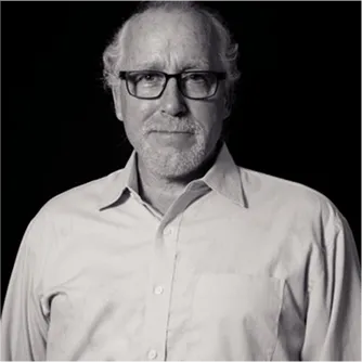 Black and white portrait of an older man wearing glasses and a light button-up shirt, looking at the camera against a dark background