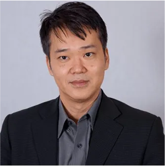 Professional man with short dark hair wearing a black suit and gray shirt against a plain background