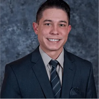 Professional man with short dark hair wearing a dark suit, striped tie, and light shirt, smiling against a studio background