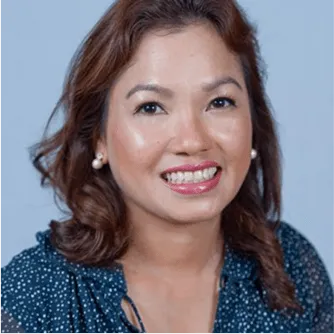 Smiling professional woman with shoulder-length hair wearing a navy blue blouse with white polka dots against a plain background