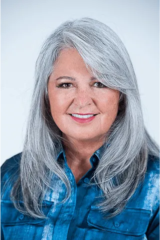 Smiling professional woman with long gray hair wearing a blue shirt against a plain background