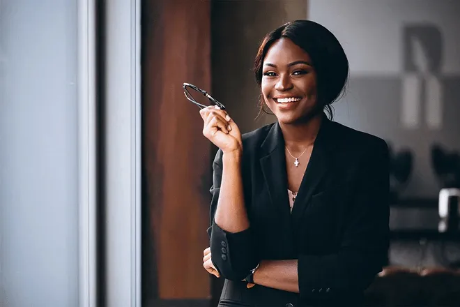 Confident professional woman in business attire smiling and holding glasses in a modern office setting