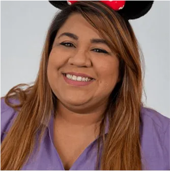 Cheerful woman with long hair wearing a purple shirt and Minnie Mouse ears headband, smiling at the camera