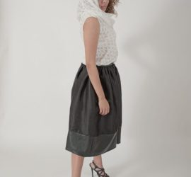 A woman in a white hooded top and black skirt stands in heels against a plain white background.