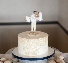 A white wedding cake with a bride and groom topper, surrounded by cupcakes with white frosting.