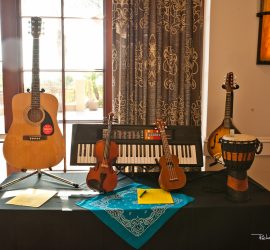 A display of various musical instruments including a guitar, keyboard, violin, ukulele, mandolin, and djembe on a table.