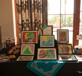 A display table with framed colorful abstract art, art supplies, and a sign reading "Drawing Gallery.