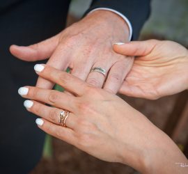 A close-up of two hands with wedding rings, one hand gently holding the other’s fingers.