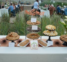 A wedding dessert table displays assorted cookies and pastries on stands, with a “Mr & Mrs” sign at the center.