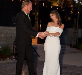 A bride in a white dress dances with a man in a suit outdoors during a wedding reception.