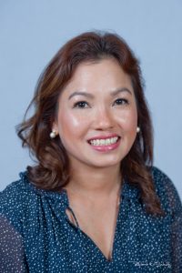 Woman with shoulder-length brown hair, wearing a navy blouse with white dots, smiling at the camera against a plain background.