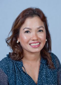 Woman with shoulder-length brown hair, wearing a navy blouse with white dots, smiling at the camera against a plain background.