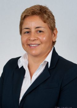 Person with short light brown hair in a dark suit and white shirt poses for a formal studio portrait against a plain background.