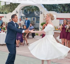 A bride and groom dance outdoors at their wedding reception while guests watch and take photos.