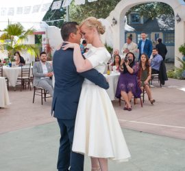 A bride and groom dance together at their wedding reception while seated guests watch in the background.