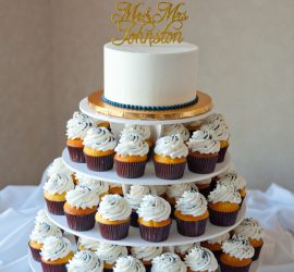 A tiered cupcake stand with a small white cake on top and cupcakes with white frosting on lower tiers.