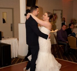 A bride and groom share their first dance together on a wooden floor in a decorated reception hall.