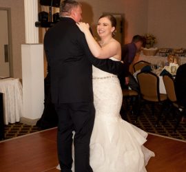 A bride and groom dance together on a wooden floor at their wedding reception in a banquet hall.