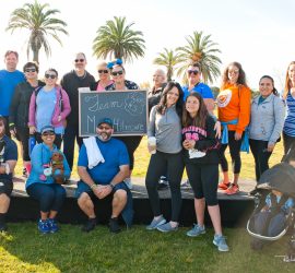 A group of people poses outdoors by a chalkboard sign reading "Team Michonne," with palm trees and grass in the background.