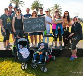 A group of people outdoors with strollers and a sign reading "Team OWEN They Cure MS!" pose for a photo.