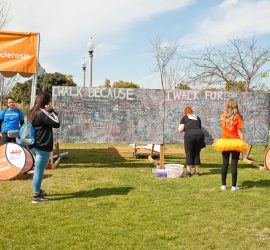 People write messages on large chalkboards at an outdoor National Multiple Sclerosis Society walk event.