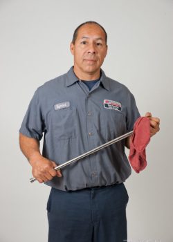 A man wearing a work uniform holds a metal rod and red cloth against a plain background.